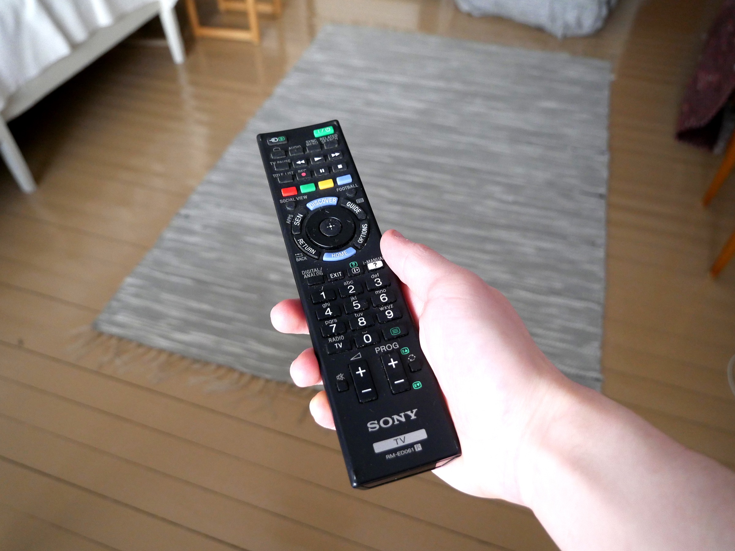Hand holding a TV remote control in a modern living room