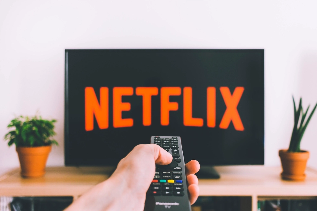 Hand pointing a remote control at a flat-panel TV in a living room